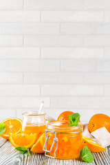 Homemade orange jam, with fresh sliced oranges and mint leaves, white wooden background copy space