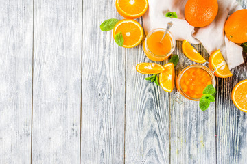 Homemade orange jam, with fresh sliced oranges and mint leaves, white wooden background copy space