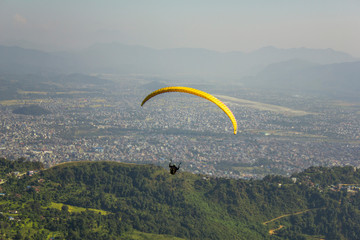 paraglider on a yellow parachute flies against the background of the city in a mountain valley in...
