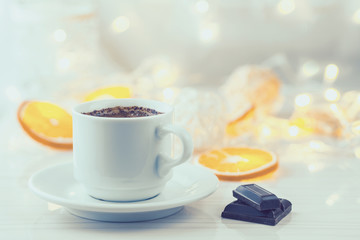 Romantic breakfast. A cup of black coffee, chocolate slices and orange slices on a background of glowing lanterns. Postcard Design