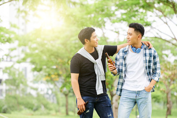 Two Asian friends spending their leisure time together outdoors with bottles of beer, they standing and talking