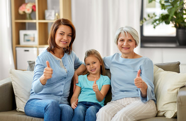 Obraz premium family, generation and female concept - portrait of smiling mother, daughter and grandmother sitting on sofa and showing thumbs up at home