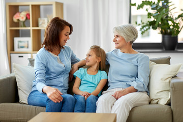 Obraz premium family, generation and female concept - smiling mother, daughter and grandmother sitting on sofa at home