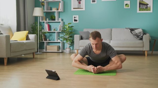 Young man following the instructions on the tablet and do the asana
