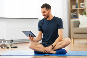 Fototapeta na wymiar sport, fitness and healthy lifestyle concept - man with tablet computer sitting on exercise mat at home