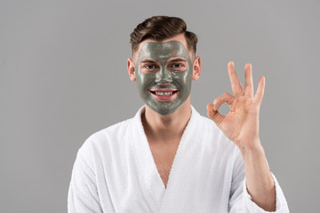 front view of smiling man in bathrobe showing okay sign isolated on grey