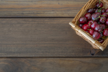 Cerezas en cesta de mimbre cuadrada realizada a mano sobre tablas de madera rústicas.