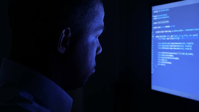 Portrait of african american man programmer coding network security software. Hacker typing code on computer screen in dark office at night