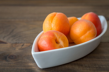 Albaricoques frescos en el cuenco blanco en los tableros de madera.