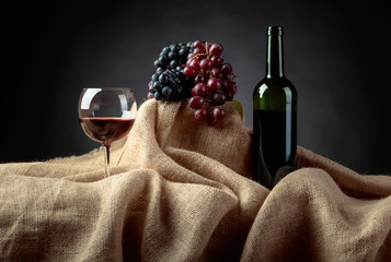 Red wine and grapes on a table covered with burlap.