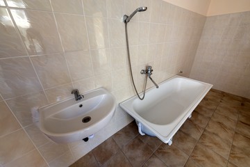 Interior of spacious light hospital or kindergarten bathroom with white bathtub, sink and tiled floor and walls.