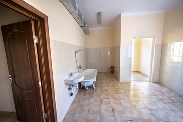 Interior of spacious light hospital or kindergarten bathroom with white bathtub, sink and tiled floor and walls.