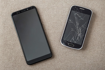 Comparison of two black mobile phones, old cellphone with cracked screen and new modern on light...