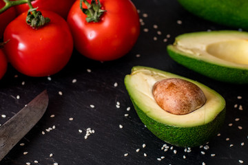 Tomatos and avocado on black table close up, colorful healthy food 