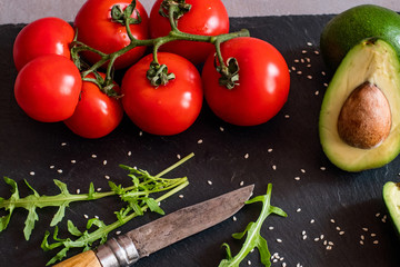 Tomatos and avocado on black table close up, colorful healthy food 