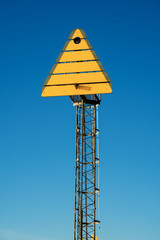 Yellow triangle sign on post in coastal landscape used as landmark orientation for shipping...