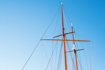 Mast on a yacht with a lot of ropes against a sunny blue sky on a summer day. Bottom view