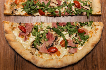 top view closeup two halves of pizza with arugula, ham, and tomatoes