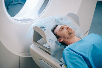 adult handsome man lying on ct scan bed during tomography test - obrazy, fototapety, plakaty