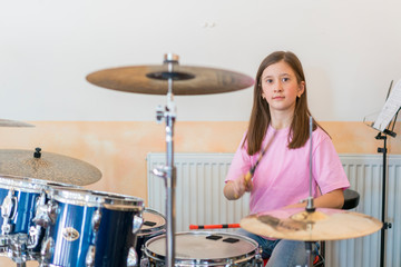Little caucasian girl drummer playing the elettronic drum kit and shuoting. Teen girls are having fun playing drum sets in music class. Close-up photo