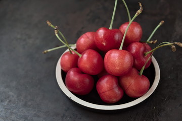 Fresh ripe cherries on a plate on a dark background. Copy space.