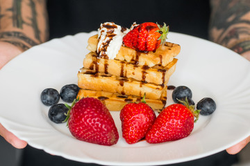 	 Belgian waffles with Strawberry and Blueberries on white plate in hands of male 