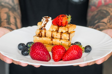 	 Belgian waffles with Strawberry and Blueberries on white plate in hands of male 