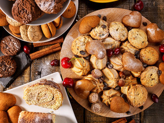 Oatmeal cookies and sand chocolate cake with cherry berry and crispy wafer rolls with cream on cutting board on wooden table in rustic style. Useful for digestion.