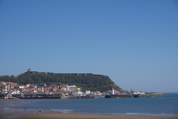 View along beachfront towards castle and harbour in Scarborough, Yorkshire, UK on a clear bright sunny blue sky day