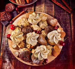 Fototapeta premium Oatmeal cookies and sand chocolate cake with cherry berry and crispy wafer rolls with cream on cutting board on wooden table in rustic style. Limitations for diabetics. Grandma's recipes.