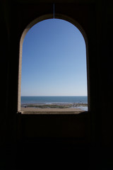 Looking out to sea through archway across empty sandy beach in Scarborough, Yorkshire, UK on a bright blue sky sunny day