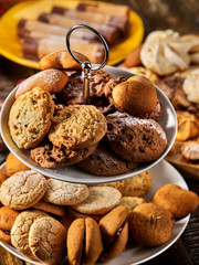 Oatmeal and nut cookies and sand biscuit on tier cake stand, crispy wafer rolls with cream on kitchen on wooden table in rustic natural style.