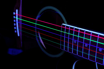 Acoustic guitar with colored luminous strings. On a black background