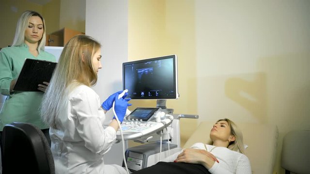 Doctor puts medical gel. She Taking A Sonogram Thyroid gland, nurse writes and helps the doctor