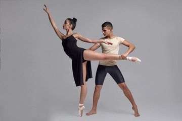 Two athletic modern ballet dancers are posing against a gray studio background.