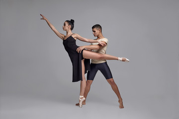 Fototapeta na wymiar Two athletic modern ballet dancers are posing against a gray studio background.