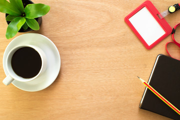 Top view. Coffee, book, pencil, employee card, and tree pot on brown wooden desk.