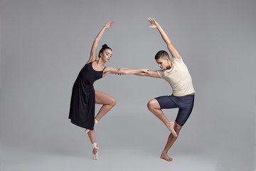 Two athletic modern ballet dancers are posing against a gray studio background.