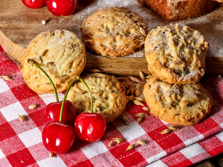 Oatmeal cookies with husk oats and cherry on kitchen cutting board gingham checkered cotton fabric on table in village style for picnic close up. Added powdered sugar. Professional recipes.