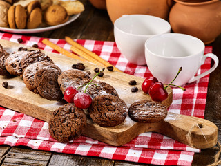 Oatmeal chocolate cookies with coffee grains and cherry straws pastry with powdered sugar on kitchen cutting board and cup of tea or coffee. Delicious and healthy food.
