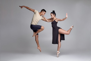 Two athletic modern ballet dancers are posing against a gray studio background.