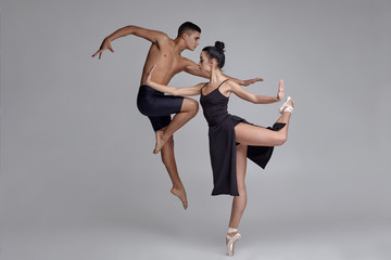 Two athletic modern ballet dancers are posing against a gray studio background. © nazarovsergey
