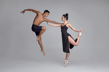 Two athletic modern ballet dancers are posing against a gray studio background.