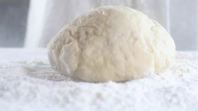 Slow motion a ball of finished raw dough falls down on a pile of flour on black background.