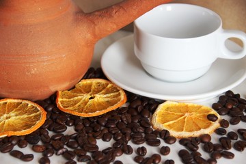brown clay dishes, white clean Cup and saucer, roasted coffee beans and dried orange on the table, close-up