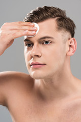 Obraz premium handsome young man wiping face with cotton pad isolated on grey