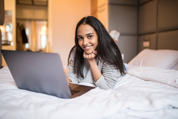 Smiling woman with her legs raised slightly in front of her laptop lying on the bed.