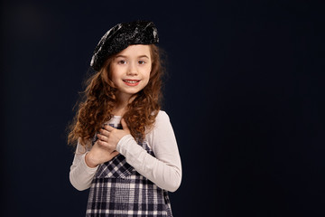 Stylish brunette kid is posing in studio on a black background. Children's fashion.