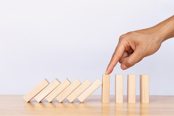 Finger stopping the domino on wooden table. Business strategy