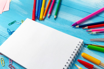 Notebook blank pages with colorful pencils, markers and pens composition Back to school concept with stationery office supplies on a blue wooden background with copy space close-up top view